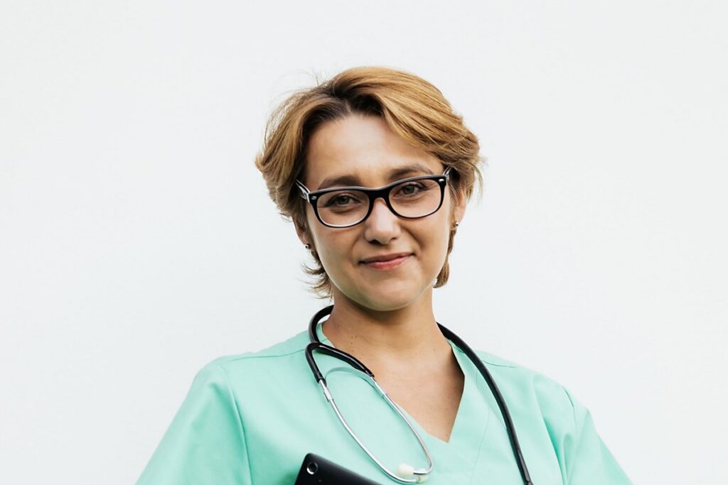 Medical assistant in scrubs with a stethoscope holding a patient records tablet