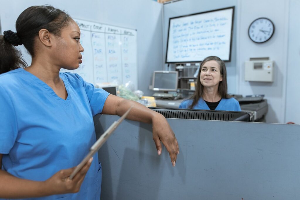 Nurse assistants in scrubs reviewing patient assignments at a hospital nurses station