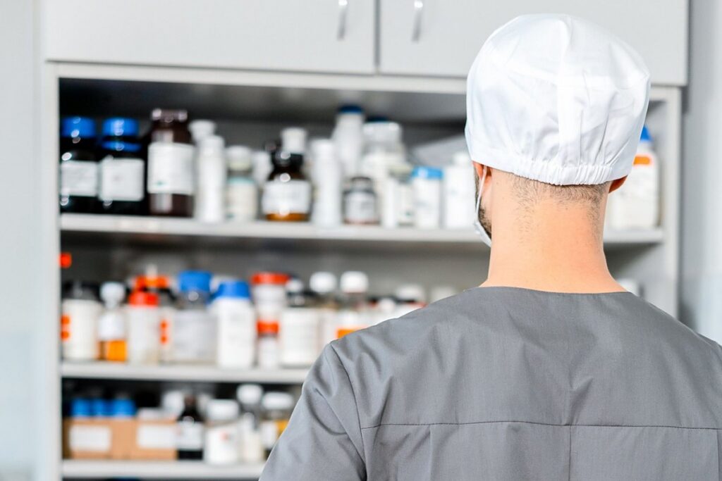 Pharmacy technician in scrubs reviewing medication stock on pharmacy shelves
